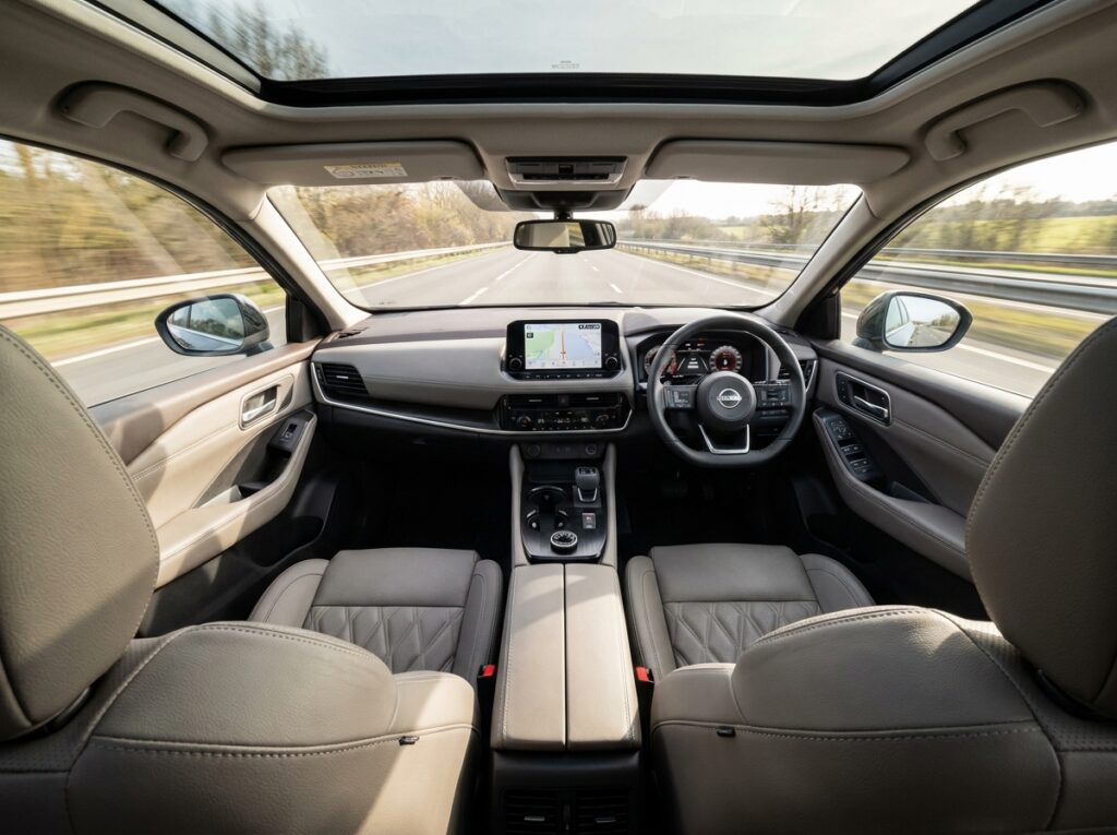 Intérieur du Nissan Qashqai vu depuis la banquette arrière, mettant en avant le tableau de bord moderne, l'écran tactile central et le toit panoramique ouvrant sur une autoroute dégagée