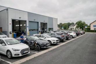 Vue extérieure d'un centre de contrôle technique en Essonne avec des véhicules en attente et un technicien en uniforme